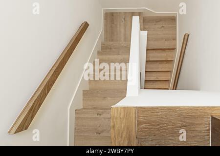 Treppen mit Eichenholztreppen mit Geländern aus demselben Material und Wänden in schlichtem weiß in einem Einfamilienhaus in verschiedenen Höhen Stockfoto