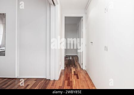 Flur eines Hauses mit weißen Einbauschränken und rötlichem Parkettboden Stockfoto