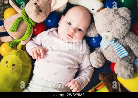 Blick von oben auf das niedliche Baby, das auf dem Boden zwischen bunten Spielzeugen liegt. Stockfoto