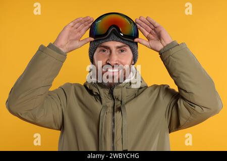 Wintersport. Glücklicher Mann in Skianzug und Brille auf orangem Hintergrund Stockfoto