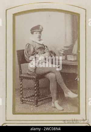 Porträt eines Mannes in einem Kostüm, der an einem Tisch mit Büchern sitzt, bezeichnet als J. Wiarda, Jan Goedeljee, 1860 - 1905 Foto. Visitenkarte dieses Foto ist Teil eines Albums. Leiden Karton. Fotografischer Trägeralbumendruck historischer Personen. Historisches Kostüm Stockfoto