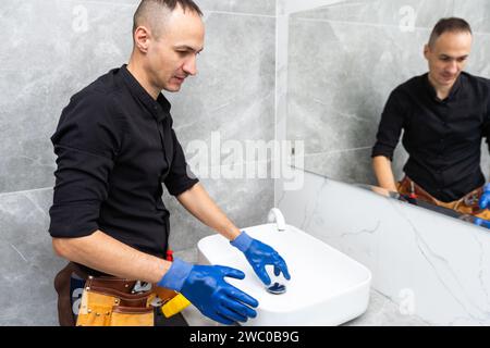 Professioneller Klempner, männlicher Arbeiter in Uniform, der Waschbecken und Wasserleitung in der neuen Wohnung installiert Stockfoto