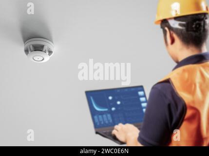 Ein Techniker oder Techniker steuert oder programmiert Rauchmelder an der Decke Stockfoto
