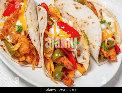 Gebackene Tex-mex-Hühnerfajitas mit gemischtem süßen Pfeffer, Zwiebeln, Sauerrahm, geriebenem Käse und weißen Maistortillas auf weißem Teller auf Holztisch, cl Stockfoto