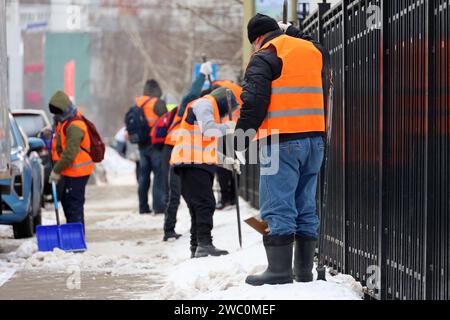 Arbeiter mit Schaufeln und Brechstangen reinigen den Gehweg, entfernen Schnee und schmelzendes Eis in der Winterstadt Stockfoto