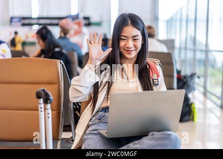 Eine junge asiatische Frau, die auf ihrem Laptop am Flughafenterminal telefoniert Stockfoto