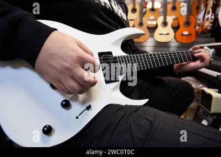 Ryazan, Russland - 9. Januar 2024: Ein Mann spielt eine weiße E-Gitarre in einem Musikgeschäft. Nahaufnahme der Hände. Selektiver Fokus Stockfoto