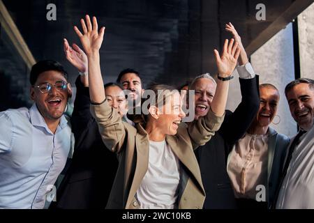 Fröhliche Kollegen feiern Erfolge, indem sie gleichzeitig die Hände heben und gemeinsam glücklich lächeln Stockfoto