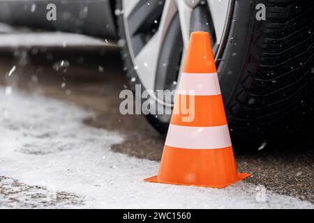 Augsburg, Bayern, Deutschland - 13. Januar 2024: Orangefarbener Kegel neben einem Autoreifen auf einer verschneiten Straße im Winter. Symbolbild der Winterreifen *** oranger Verkehrskegel neben einem Autoreifen im Winter bei einer mit Schnee bedeckten Straße. Symbolbild Winterreifen Stockfoto