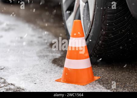 Augsburg, Bayern, Deutschland - 13. Januar 2024: Orangefarbener Kegel neben einem Autoreifen auf einer verschneiten Straße im Winter. Symbolbild der Winterreifen *** oranger Verkehrskegel neben einem Autoreifen im Winter bei einer mit Schnee bedeckten Straße. Symbolbild Winterreifen Stockfoto