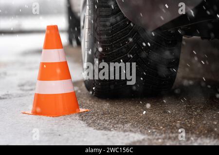Augsburg, Bayern, Deutschland - 13. Januar 2024: Orangefarbener Kegel neben einem Autoreifen auf einer verschneiten Straße im Winter. Symbolbild der Winterreifen *** oranger Verkehrskegel neben einem Autoreifen im Winter bei einer mit Schnee bedeckten Straße. Symbolbild Winterreifen Stockfoto