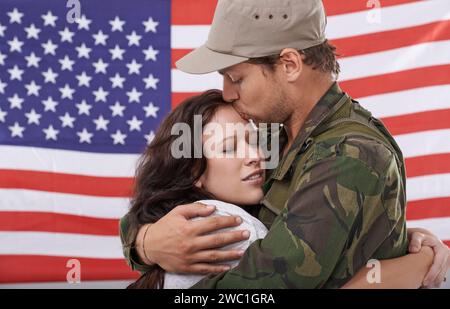 Amerikanischer Soldat küsst Frau, Wiedersehen nach dem Krieg und Umarmung, um Helden mit Liebe und Flagge willkommen zu heißen. Der Mann der Armee vereint sich mit seinem Partner, Militärveteran in Uniform Stockfoto