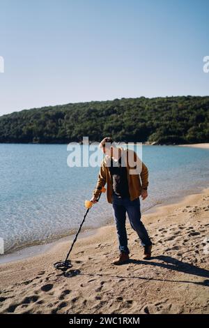 Ein junger Mann mit einem Metalldetektor läuft am Sandstrand entlang Stockfoto