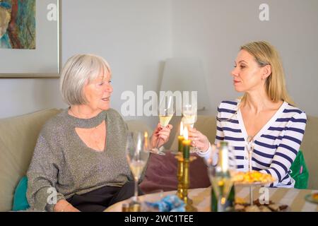 Mutter und Tochter sitzen zusammen auf der Couch und tosten eine schöne Feier mit Champagner Stockfoto