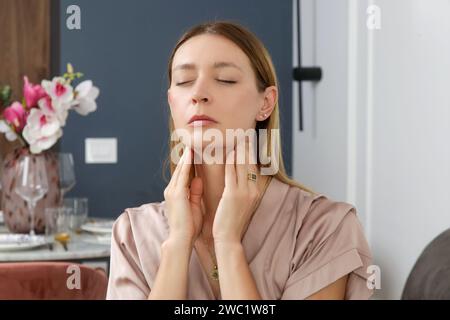 Eine kaukasische Frau, die ihren Hals berührt. Halsschmerzen, Erkältung, Grippe, Tonsillitis oder Schilddrüsenproblem Stockfoto