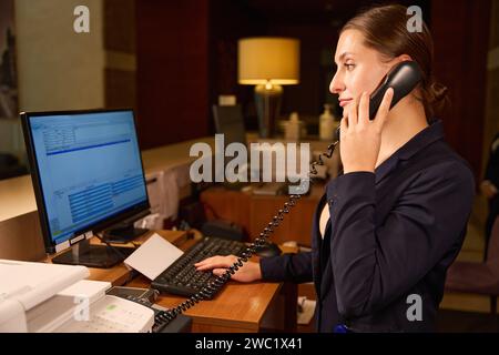 Seitenfoto des Rezeptionisten beim Telefonieren und Tippen am Computer Stockfoto