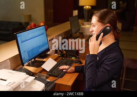Eine ruhige Frau an der Rezeption spricht am Telefon und tippt am Computer Stockfoto