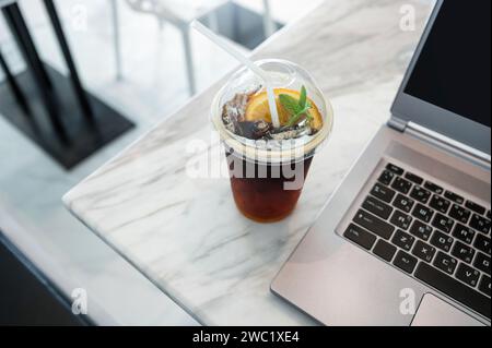 Orange Americano Eiskaffee mit modernem Laptop auf Marmorschreibtisch Stockfoto
