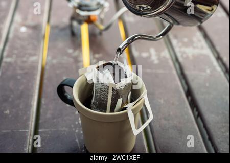 Gießen Sie heißes Wasser aus dem Wasserkocher in gemahlenen Kaffee auf einer Tasse. Morgens tropfenden Kaffee zubereiten Stockfoto