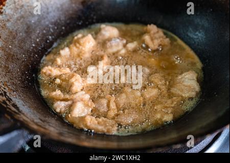 Knusprig gebratenes Hühnerfleisch mit kochendem Öl in einer traditionellen, gealterten Pfanne auf einem Gasherd braten Stockfoto