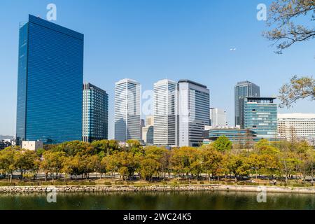 Blick vom Schlosspark Osaka auf den Osaka Business Park mit dem Crystal Tower, Panasonic Twin Towers und anderen. Frühling, blauer Himmel, Flugzeugflug. Stockfoto