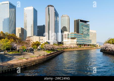 Blick von der Shinshigino Bridge of Osaka Business Park mit dem IMP-Gebäude, Panasonic Twin Towers und anderen, mit dem Okawa Fluss und Kirschblüten. Stockfoto