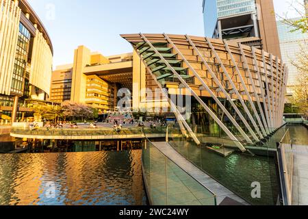 Umekita Ship Hall und Wasserspiel mit dem Nordtor der Stadt Osaka Station dahinter, beleuchtet von der untergehenden Sonne (ungesehen), im Frühling. Stockfoto