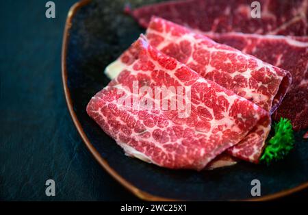 Geschnittenes Wagyu-Rindfleisch für Yakiniku auf Platte auf schwarzem Hintergrund, japanisches Premium-Fleischkonzept Stockfoto