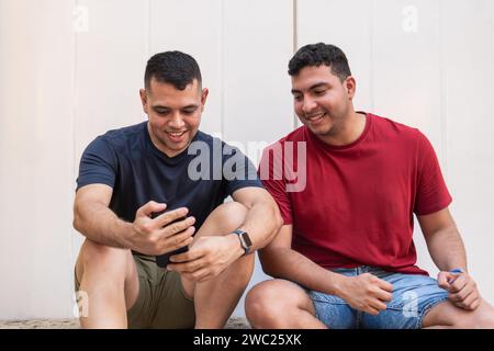 Lateinische Freunde sitzen und lächeln, während sie gemeinsam ein Smartphone betrachten Stockfoto