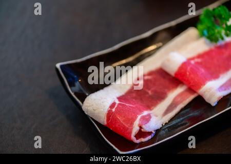 In Scheiben geschnittenes Wagyu marmoriertes Rindfleisch für Yakiniku auf Platte auf schwarzem Hintergrund, japanisches Premium-Fleischkonzept Stockfoto