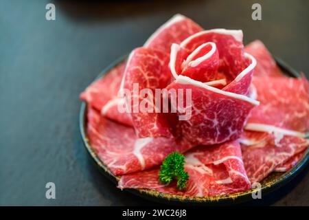 In Scheiben geschnittenes Wagyu marmoriertes Rindfleisch für Yakiniku auf Platte auf schwarzem Hintergrund, japanisches Premium-Fleischkonzept Stockfoto