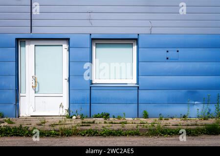 Details der blauen Fassade aus Aluminiumplatten mit Türen und Fenstern am Industriebau Stockfoto