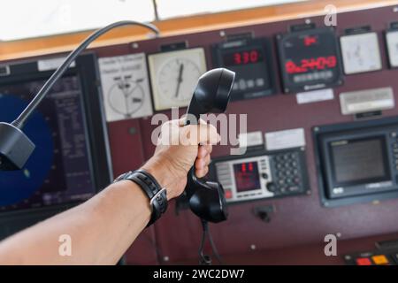 Navigationsbedienfeld und UKW-Funkgerät mit Hand. Funkkommunikation auf See. Arbeiten an der Schiffsbrücke. Stockfoto