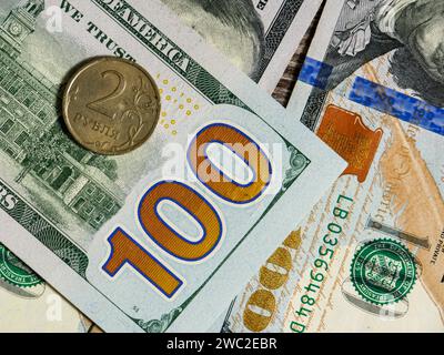 Gelbe russische Münze im Wert von 2 Rubel auf dem Hintergrund von Dollarscheinen. Dollar-Banknoten und -Münzen. Stockfoto