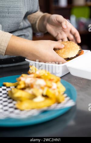 Verpacken eines Hamburger und Pommes in einem Behälter für Lieferung, schnelle und ungesunde Lebensmittel, Arbeit und Geschäft Stockfoto