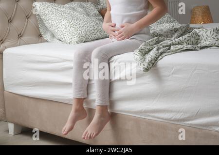 Kleines Mädchen, das im Schlafzimmer mit Magenschmerzen liegt. Hände auf den Bauch. Stockfoto