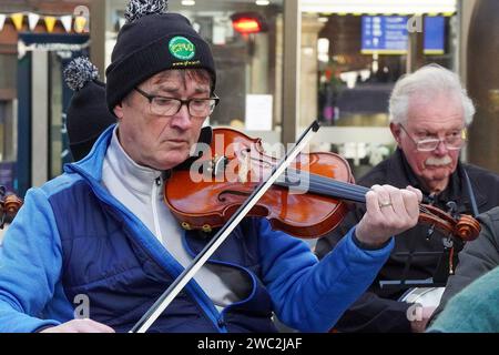 Glasgow, Großbritannien. Januar 2024. Schüler und Tutoren des Glasgow Fiddle Workshop, bekannt als „GFW“, einer schottischen Wohltätigkeitsorganisation, die 1992 als Geigen-Workshop begann, spielten für Reisende im Central Railway Station in Glasgow, Schottland. Der Workshop unterstützt und fördert die Teilnahme an traditioneller Musik und bietet Unterricht in verschiedenen Instrumenten wie Akkordeon, Geige, Banjo und Mandoline. Quelle: Findlay/Alamy Live News Stockfoto