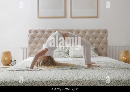 Süßes kleines Mädchen, das eine Yoga-Rad-Pose auf dem Bett macht Stockfoto