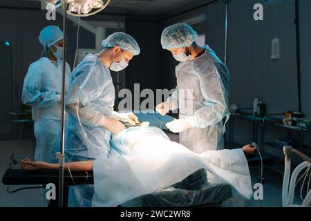 Wide Shot von verschiedenen Team von professionellen männlichen Chirurgen und weiblichen Krankenschwestern führt invasive Chirurgie am Patienten im Krankenhaus. Afroamerikanische Assistentin Stockfoto