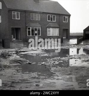 1960er Jahre, historische, neu gebaute Doppelhaushälften, mit Auffahrten, in der Ecke eines ländlichen Wohnsitzes, Bürgersteig und Straßenbauarbeiten noch nicht fertiggestellt, England, Großbritannien. Stockfoto