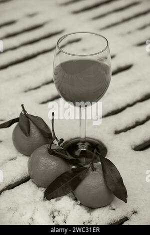 Glas frisch gepressten Bio-Mandarinensaft auf schneebedeckten Tisch im Garten und Mandarinenfrüchte. Gesunder Lebensstil Hintergrund. Sepia-Foto. Stockfoto