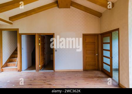 Wohnzimmer mit Holzbalkendecke und Türen, die zu anderen Zimmern in einem zweistöckigen verlassenen Haus führen Stockfoto