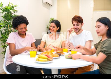 Multi-ethnische Freunde essen gesundes Frühstück zusammen zu Hause sitzen und Tisch teilen Stockfoto