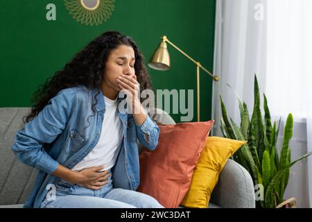 Eine beunruhigte junge Frau, die sich auf einer Couch übel fühlt, übergibt ihren Mund und versucht, den Drang zu Erbrechen zu unterdrücken. Stockfoto