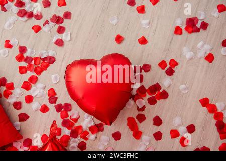 Auf Holzlaminatboden liegt ein Herzballon aus roter Folie zwischen roten, weißen Rosenblättern. Grußkarte, Platz für Teig, Kopierraum, Mock Up. Top-Film Stockfoto