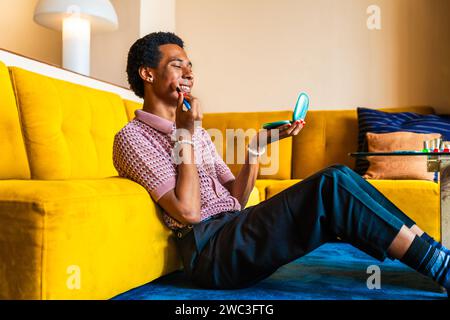 Fließender junger Mann, der zu Hause Crossdressing trägt, LGBTQ- und Diversity-Konzepte - hispanisches nicht binäres männliches Porträt in einer bunten Wohnung Stockfoto