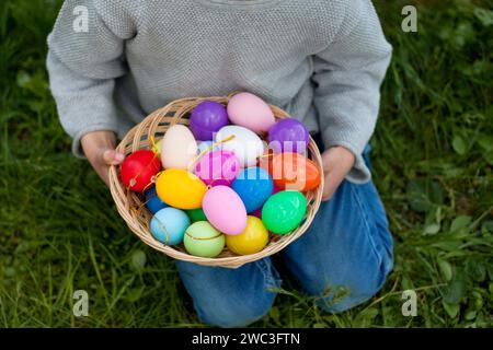 Frohe ostern. Ostereierjagd. Nahaufnahme eines Korbes voller bunter Eier in den Händen des Kindes. Lustige Ostertradition. Im Freien, Frühling Stockfoto