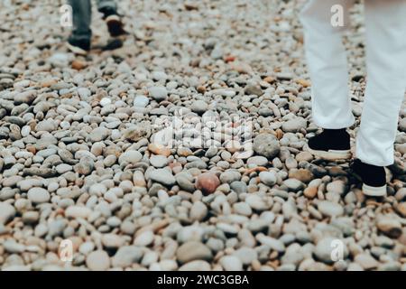 Weiße Kiessteine am Strand. Menschen in weißen Kleidern in klassischem Luxusstil spazieren am Meer. Die Reisenden auf einem Spaziergang. Schifffahrt. Stockfoto