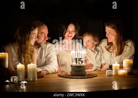 Niedliches 15-jähriges Mädchen, das sich wünscht, bevor es Kerzen auf ihre Geburtstagskuche bläst. Fünfköpfige Familie feiert Kindergeburtstag. Geburtstags-Traditionen Stockfoto