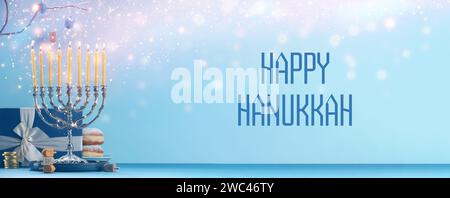 Happy Hanukkah. Menora, Donuts, Dreidels und Geschenk auf blauem Tisch, Banner-Design Stockfoto